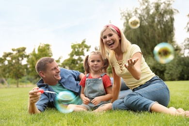 Photo of Happy family blowing soap bubbles in park on green grass