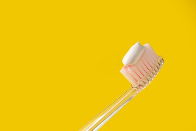 Photo of Brush with toothpaste on yellow background, closeup. Space for text
