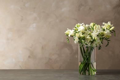 Photo of Beautiful freesia flowers in vase on grey table. Space for text