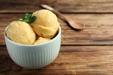 Photo of Delicious yellow ice cream in bowl on wooden table, space for text