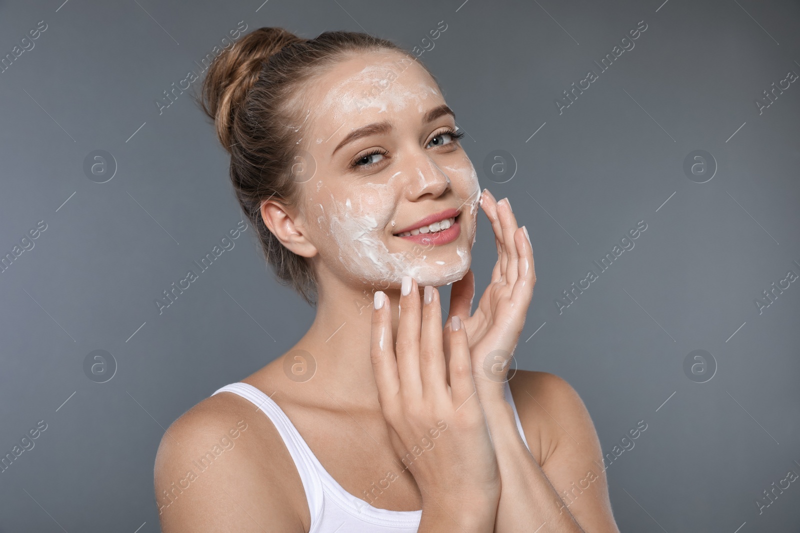 Photo of Young woman washing face with soap on grey background