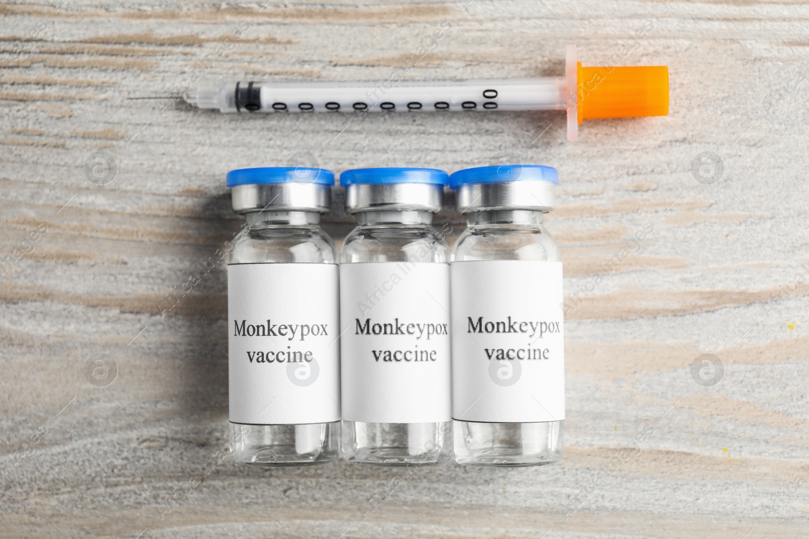 Photo of Monkeypox vaccine in glass vials and syringe on wooden table, flat lay