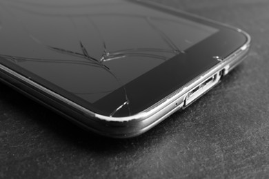 Smartphone with cracked screen on black table, closeup. Device repair