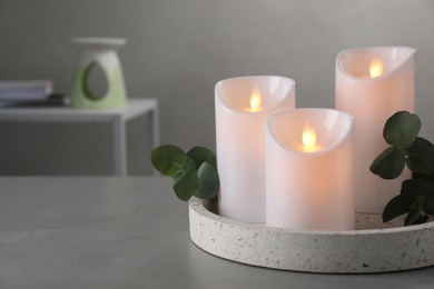 Photo of Decorative LED candles and eucalyptus on grey table, space for text