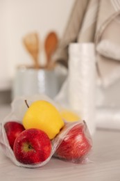 Photo of Plastic bag with fresh apples on white table, closeup. Space for text