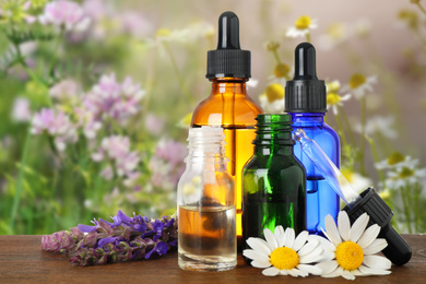 Image of Bottles of essential oils and wildflowers on wooden table against blurred background