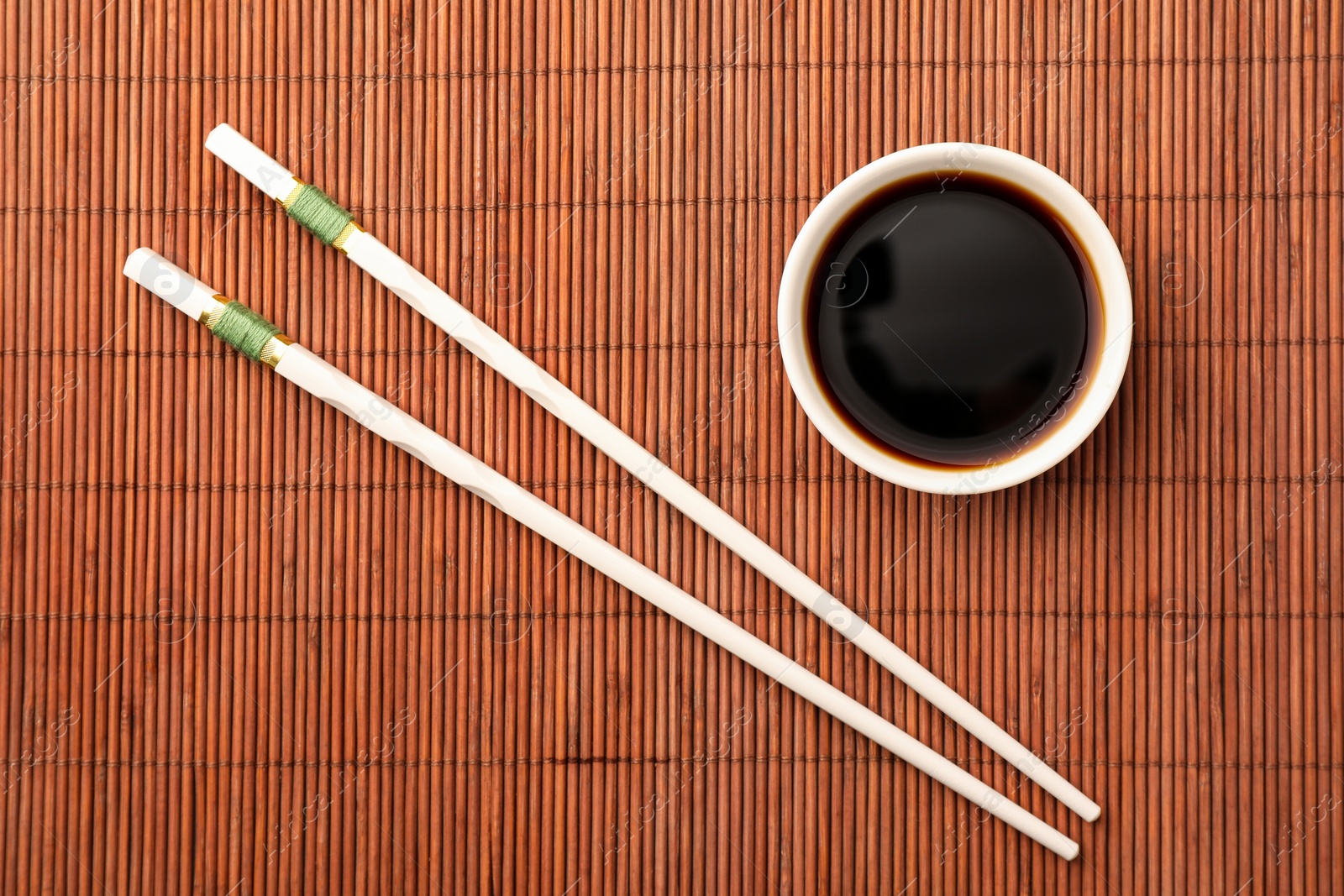 Photo of Bowl of soy sauce and chopsticks on bamboo mat, flat lay