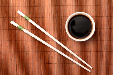 Photo of Bowl of soy sauce and chopsticks on bamboo mat, flat lay