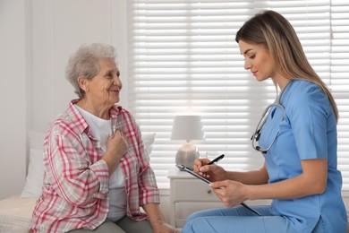 Photo of Young caregiver examining senior woman in room. Home health care service