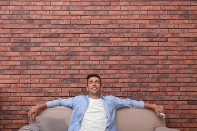 Photo of Young man relaxing under air conditioner on brick wall at home