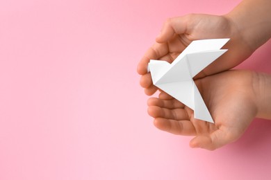 Photo of Origami art. Child holding paper bird on pink background, top view. Space for text