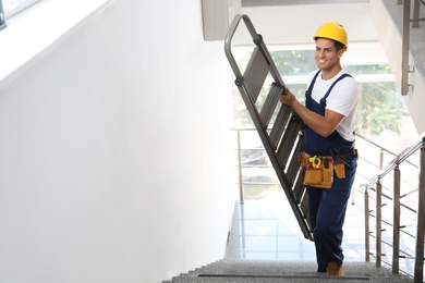 Photo of Professional builder carrying metal ladder up stairs