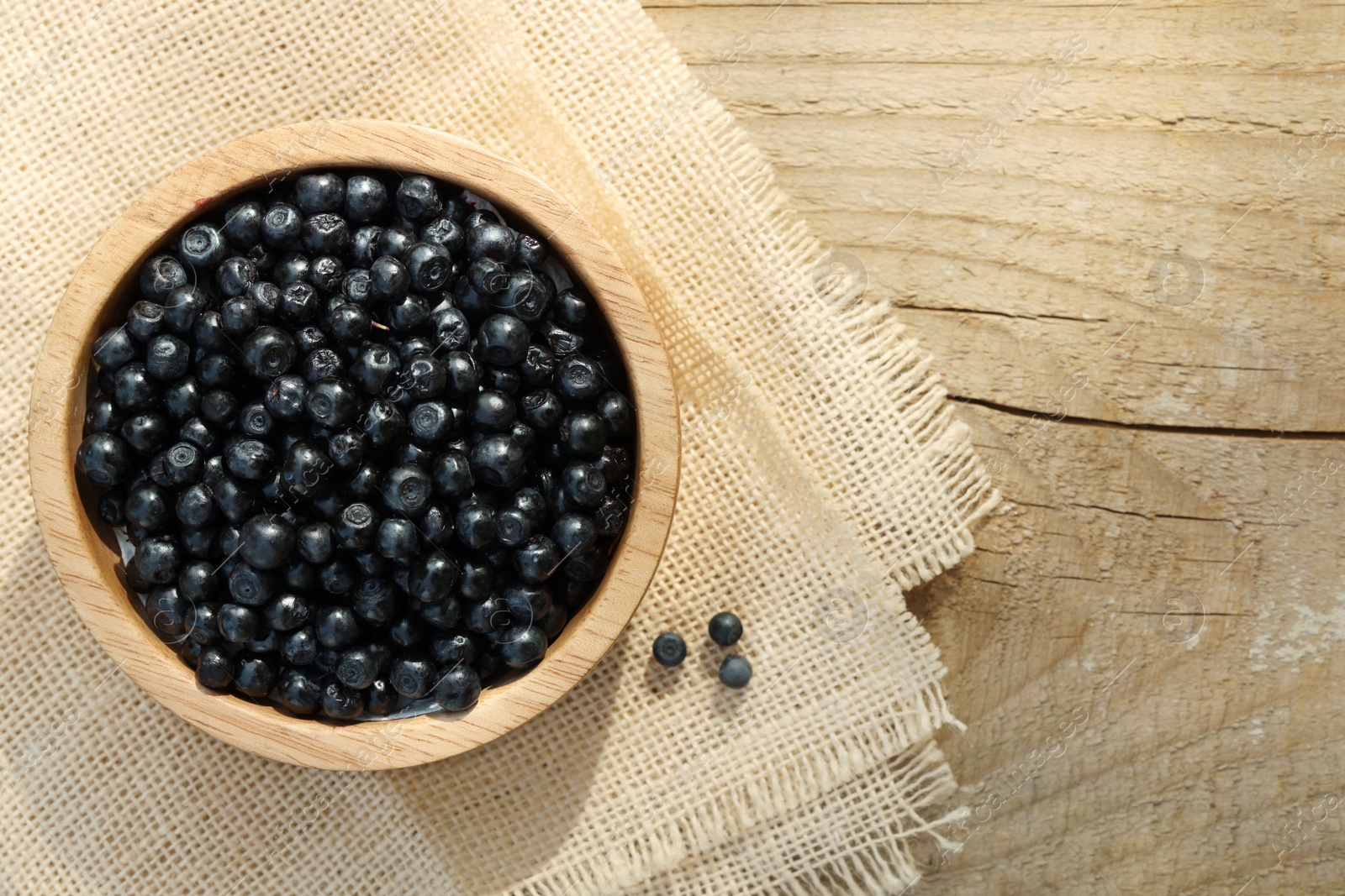 Photo of Bowl of delicious bilberries on wooden table, top view. Space for text