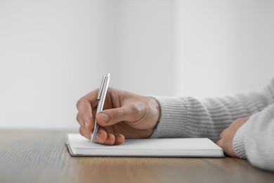 Photo of Man writing in notebook at wooden table, closeup