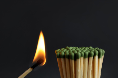 Photo of Burning match near unlit ones on dark background, closeup