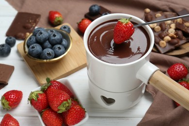 Photo of Dipping fresh strawberry in fondue pot with melted chocolate at white wooden table