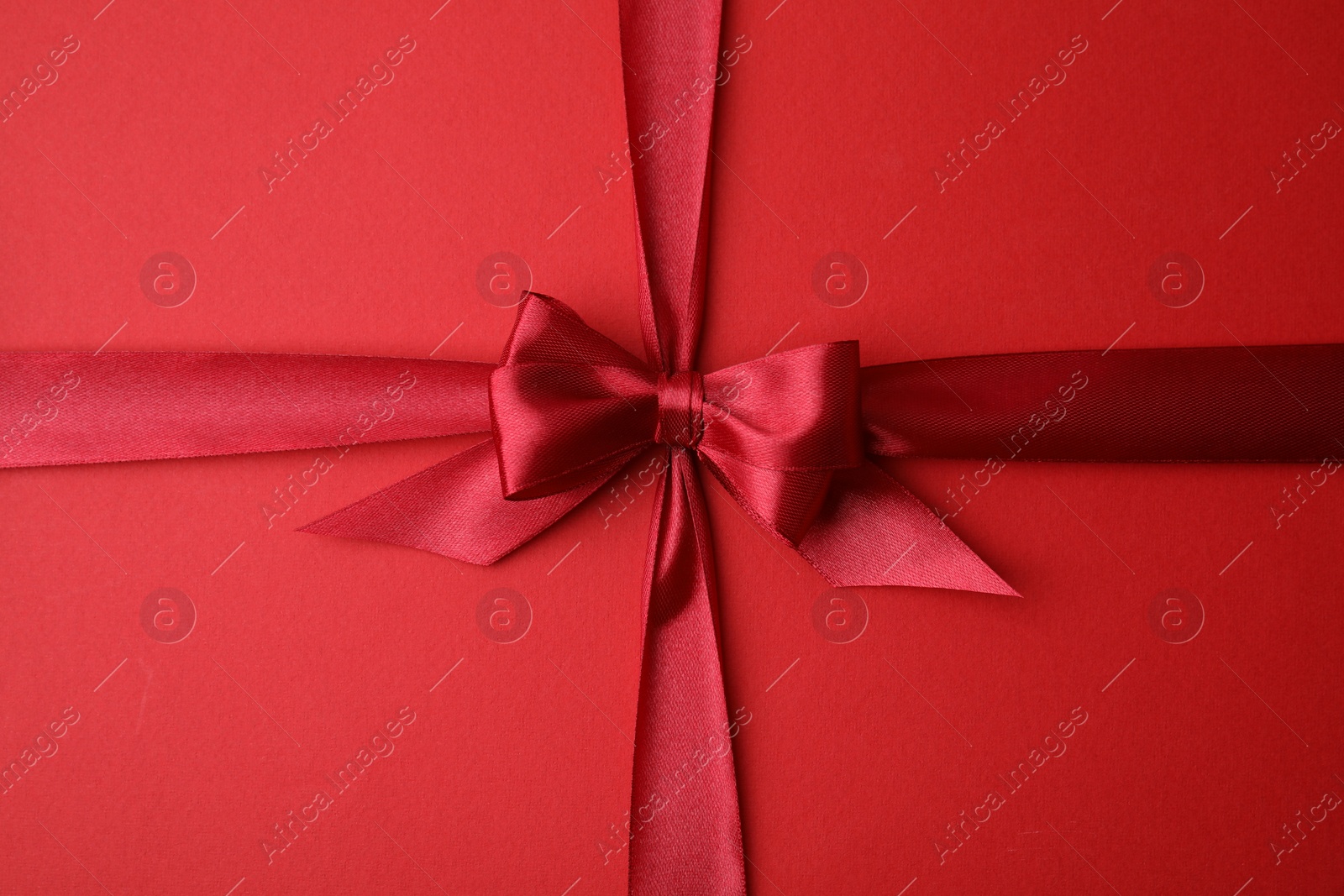 Photo of Bright satin ribbon with bow on red background, top view