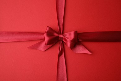 Bright satin ribbon with bow on red background, top view