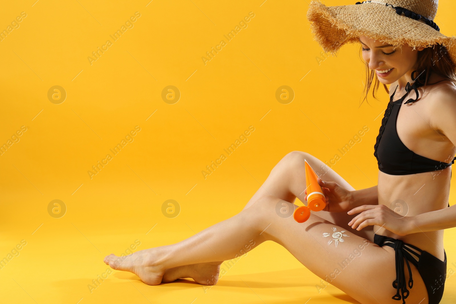 Photo of Woman applying sun protection cream on leg against yellow background. Space for text