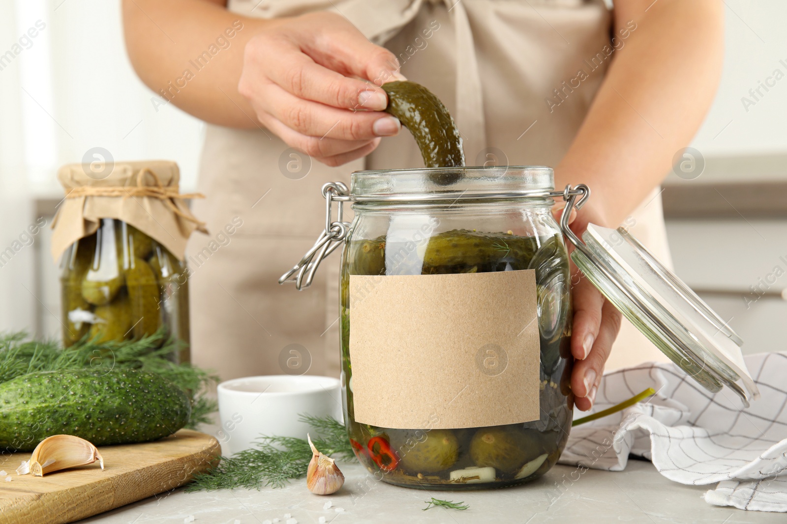 Photo of Woman taking pickled cucumber from jar at table in kitchen, closeup view. Space for text