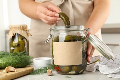 Photo of Woman taking pickled cucumber from jar at table in kitchen, closeup view. Space for text