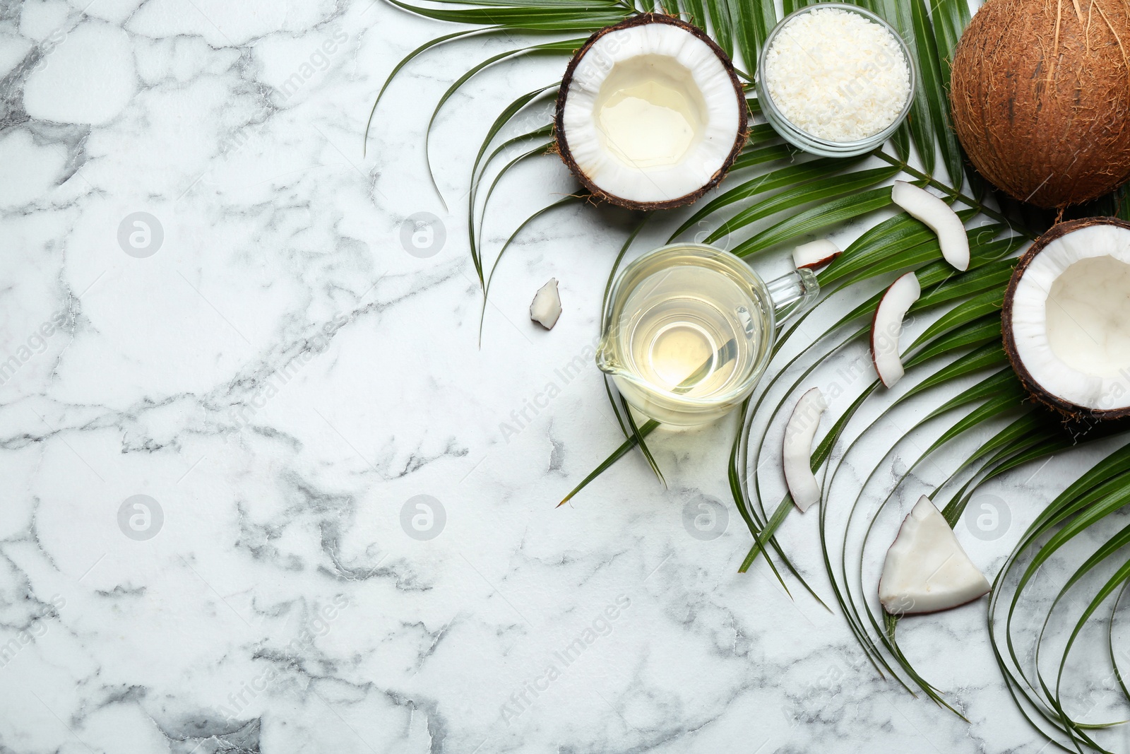 Photo of Jug of natural organic oil and coconuts on marble background, flat lay. Space for text