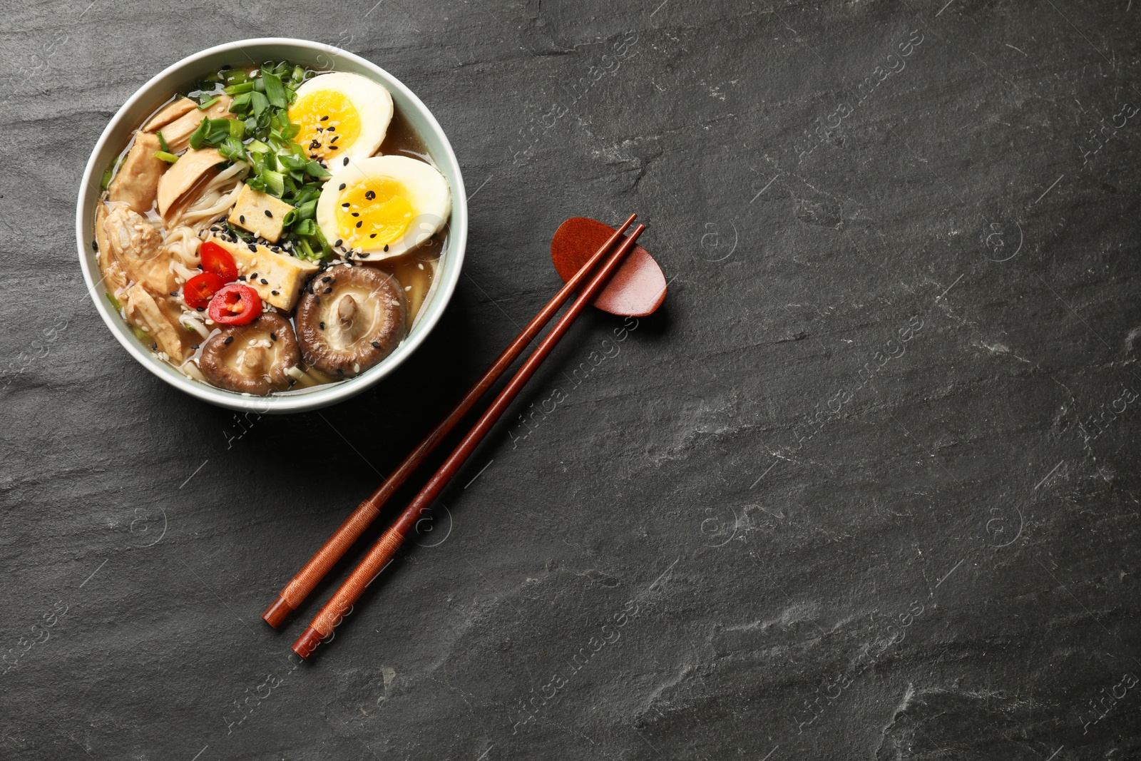 Photo of Noodle soup. Bowl of delicious ramen, ingredients and chopsticks on black table, flat lay. Space for text