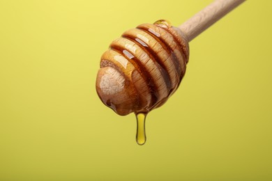 Photo of Delicious honey flowing down from dipper against yellow background, closeup