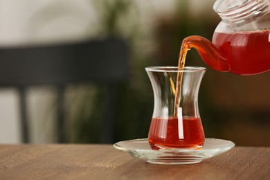 Photo of Pouring tasty Turkish tea into glass on wooden table indoors, space for text
