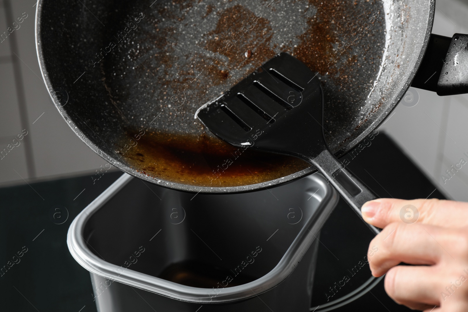 Photo of Woman pouring used cooking oil from frying pan into container, closeup
