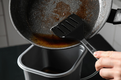 Photo of Woman pouring used cooking oil from frying pan into container, closeup