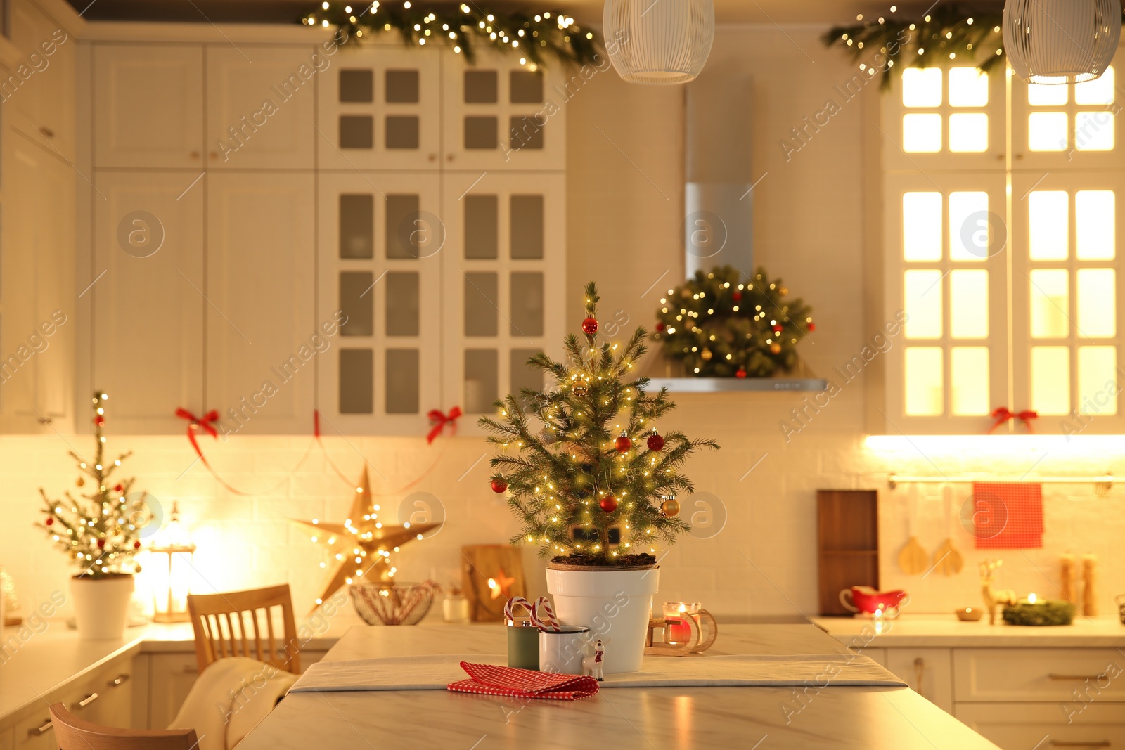 Photo of Small Christmas tree decorated with baubles and festive lights in kitchen