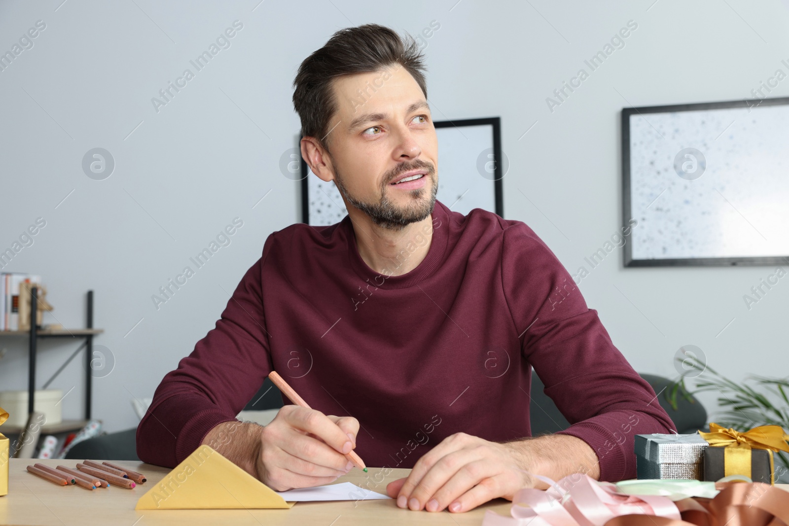 Photo of Man writing message in greeting card at wooden table in room