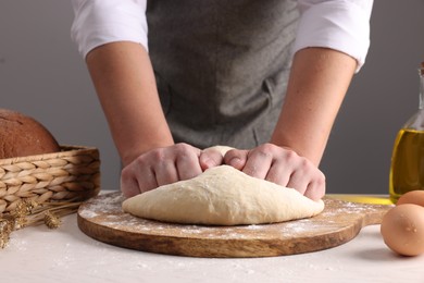 Photo of Man kneading dough at table near grey wall, closeup