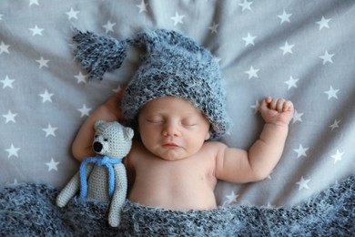 Cute newborn baby in warm hat with toy sleeping on bed, top view