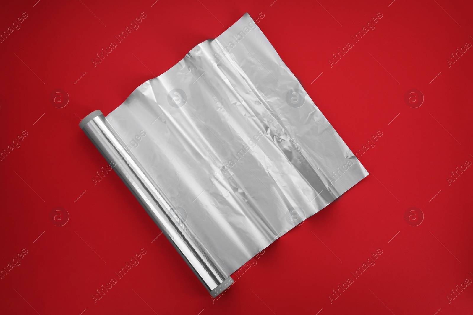 Photo of Roll of aluminum foil on red background, top view