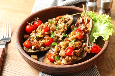 Photo of Bowl with tasty stuffed eggplants on wooden table