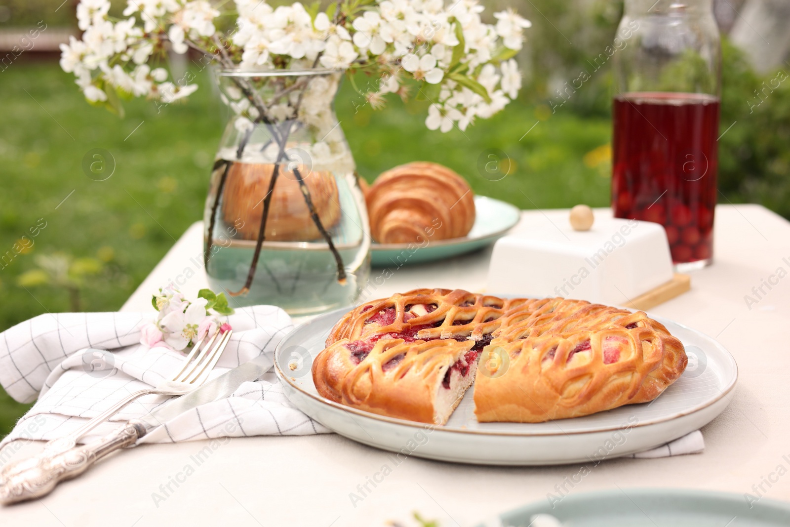 Photo of Stylish table setting with beautiful spring flowers, fruit drink and pie in garden