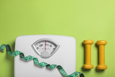 Photo of Weight loss concept. Scales, dumbbells and measuring tape on green background, flat lay. Space for text