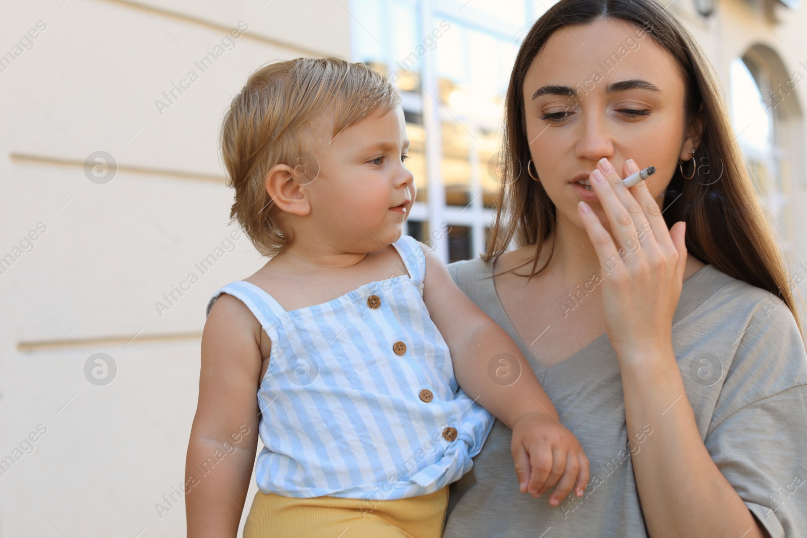 Photo of Mother with cigarette and child outdoors. Don't smoke near kids