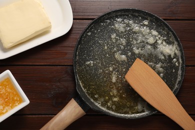 Photo of Melted butter in frying pan and spatula on wooden table, flat lay