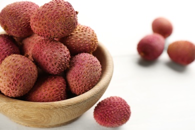 Photo of Fresh ripe lychees in bowl on white wooden table, closeup. Space for text