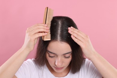 Photo of Woman with comb examining her hair and scalp on pink background. Dandruff problem
