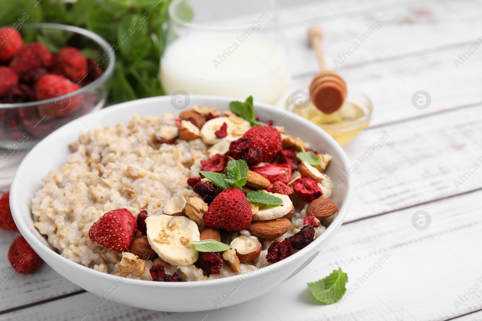 Photo of Delicious oatmeal with freeze dried berries, banana, nuts and mint on white wooden table, closeup