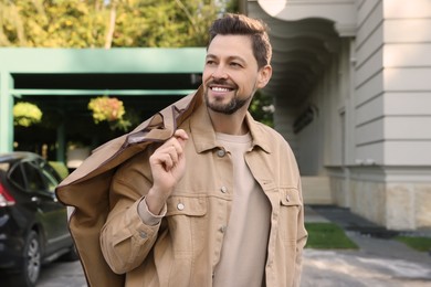 Attractive happy man holding garment cover with clothes outdoors. Dry cleaning service