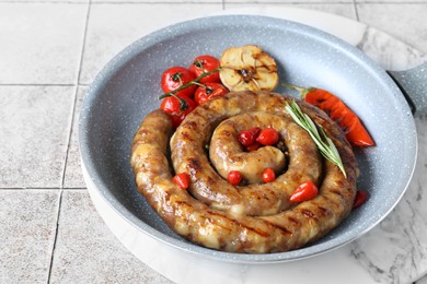 Delicious homemade sausage with garlic, tomatoes, rosemary and chili in frying pan on light tiled table, closeup