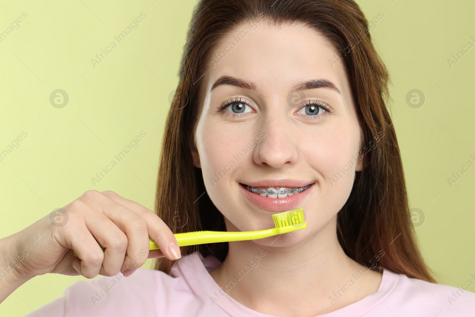 Photo of Smiling woman with dental braces cleaning teeth on light green background