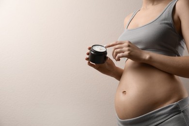 Pregnant woman with cosmetic product on beige background, closeup. Space for text