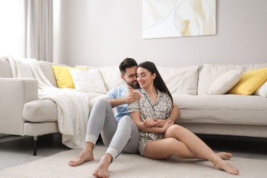 Photo of Happy couple in pajamas sitting on floor at home