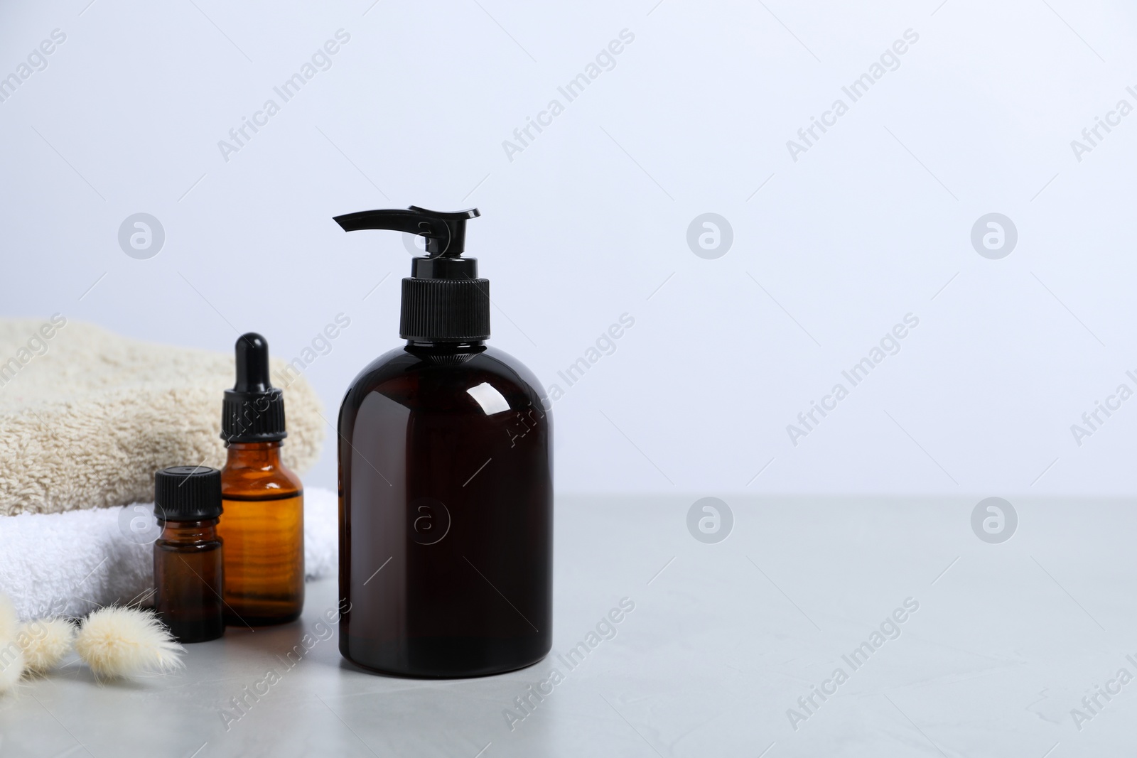 Photo of Bottles with different cosmetic products, dry decorative spikes and soft towels on light grey table, space for text